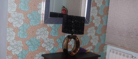 Une pièce avec un papier peint à motifs floraux, un miroir, une petite table et un radiateur.