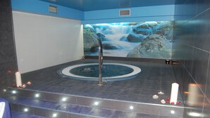 A spa area with a hot tub, a waterfall mural, and candles on the floor. - Hotel & Spa Arha Potes (Potes)