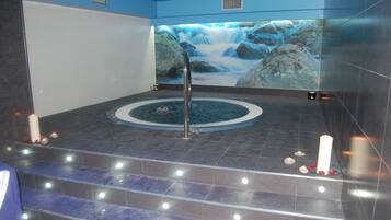 Un área de spa con un jacuzzi, un mural de cascada y velas en el suelo.