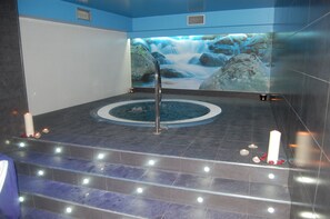 A spa area with a hot tub, a waterfall mural, and candles on the floor. - Hotel & Spa Arha Potes (Potes)