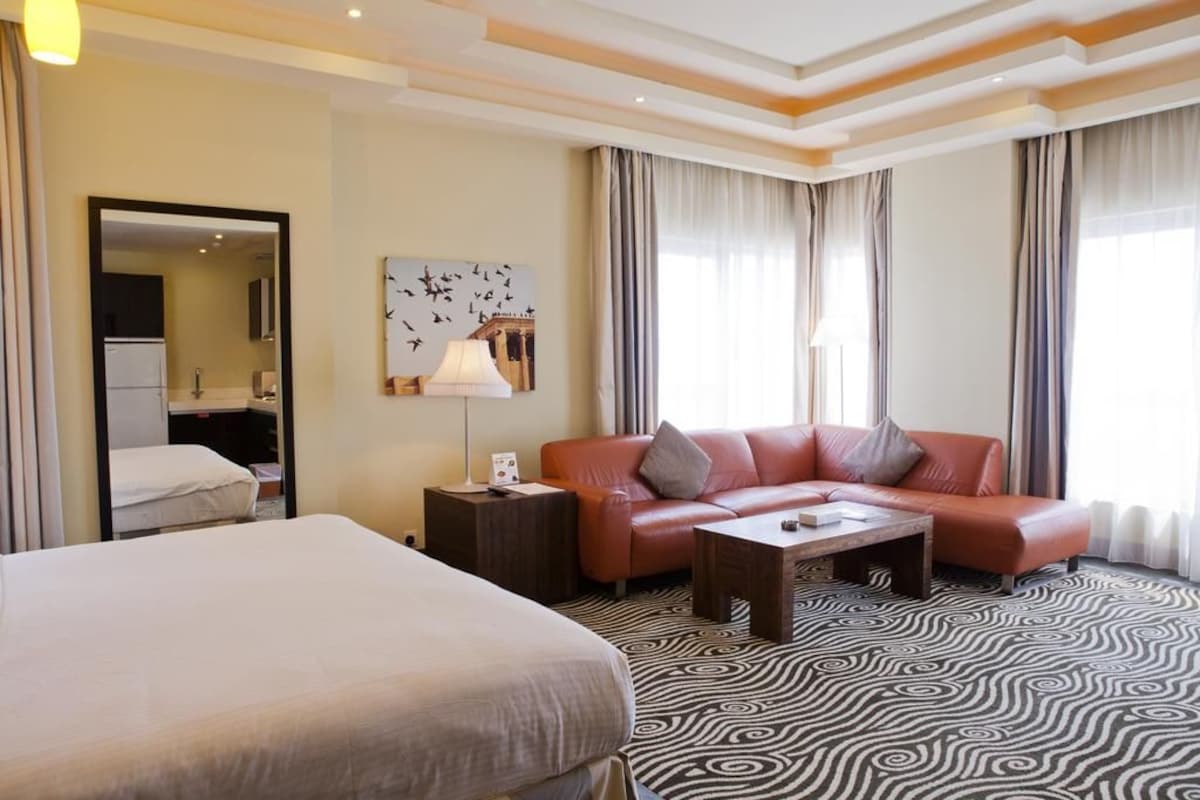 Quarto de hotel com cama, sofá, mesa de centro e um quadro na parede.