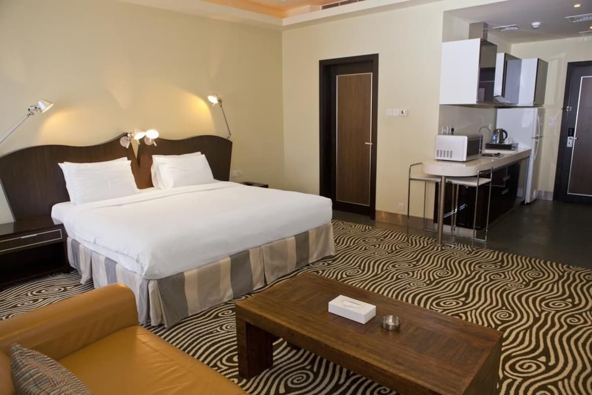 Quarto de hotel com uma cama grande, uma secretária pequena, uma cadeira e uma mesa de centro.