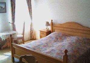 A bedroom with a wooden bed, a bedside table with a lamp, a chair, and a window with curtains. - Landgasthof & Hotel Krone (Konigsbach-Stein)