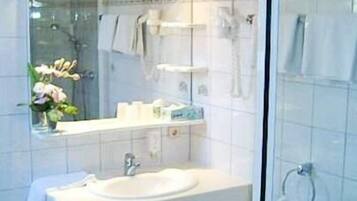 Ein Badezimmer mit weißem Waschbecken, einem Spiegel und einer Duschkabine aus Glas.
