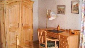 Una habitación con un armario de madera, un escritorio con una silla y una cama con colcha estampada.