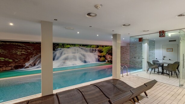 A pool area with a waterfall mural, lounge chairs, and a glass-enclosed dining area. - Banyan Hotel (Sankt Anton am Arlberg)