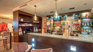 A bar area with a counter, bar stools, and shelves stocked with various bottles and glasses. - Banyan Hotel (Sankt Anton am Arlberg)