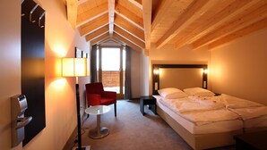 A hotel room with a wooden ceiling, a bed, a red chair, a small table, and a wall-mounted lamp. - Banyan Hotel (Sankt Anton am Arlberg)