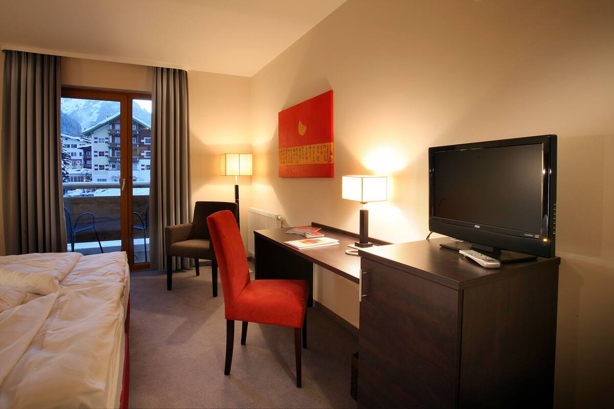 A hotel room with a bed, a desk with a computer, a TV, and a chair.