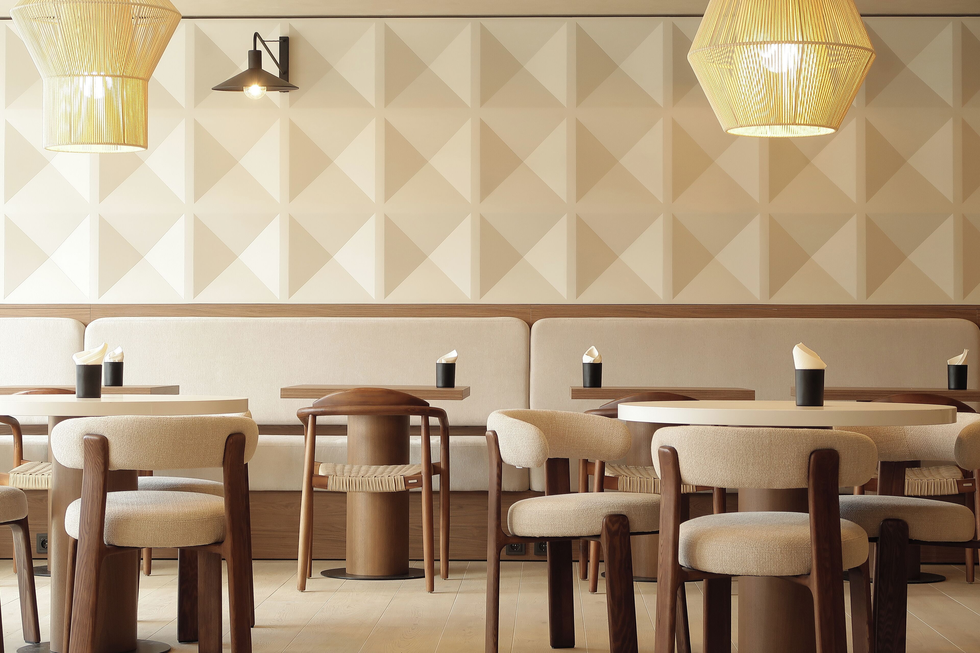 A modern dining area with wooden chairs and tables, geometric patterned walls, and pendant lighting.