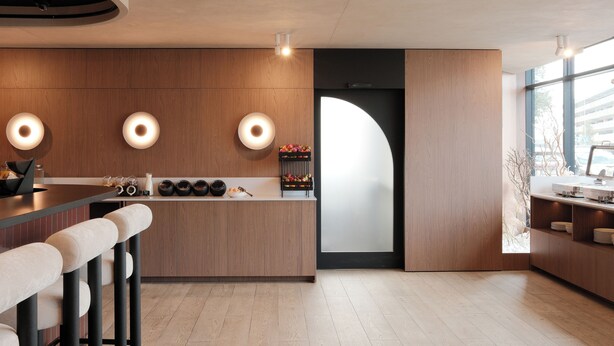 Una cocina moderna con armarios de madera, una isla central, taburetes de bar e iluminación colgante.