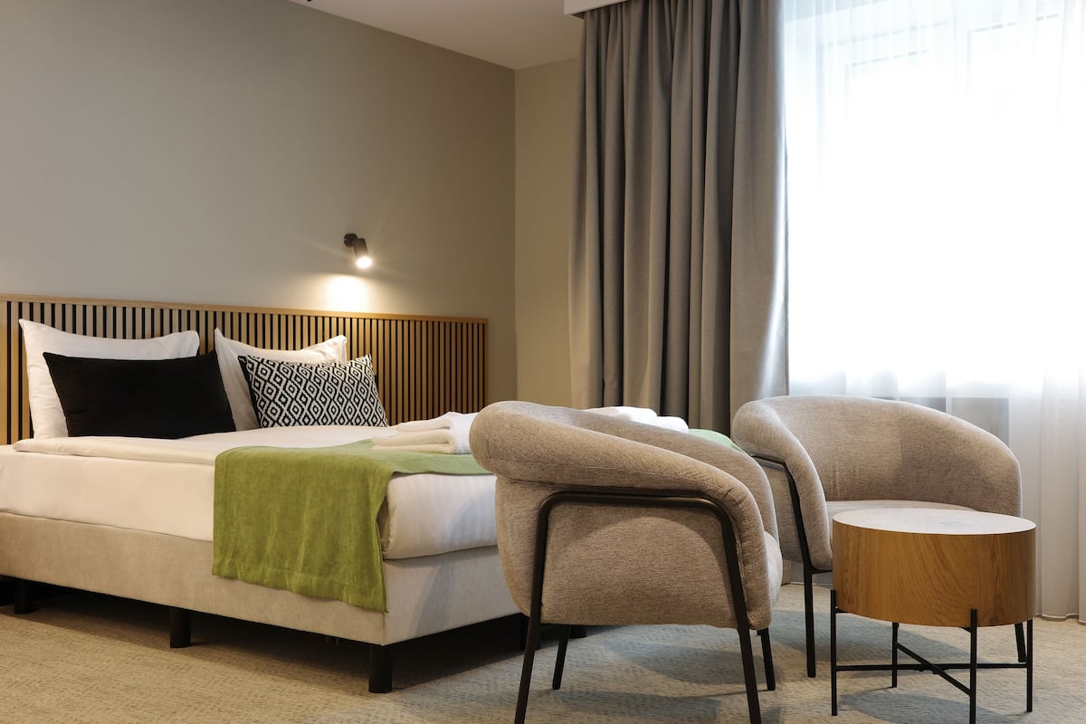 A hotel room with a bed, two chairs, a small round table, and a lamp.