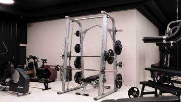 Un gimnasio con una estructura para sentadillas, banca de pesas y diversas máquinas de pesas.
