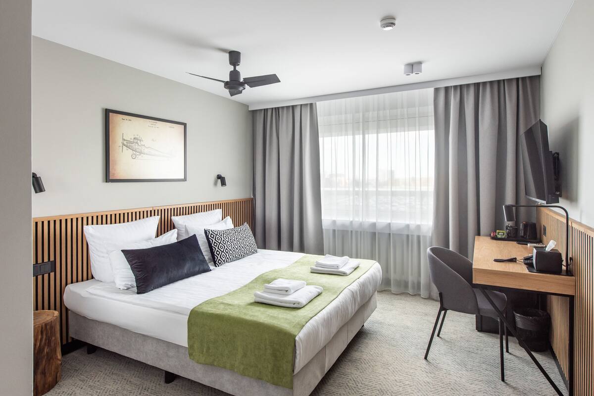 A hotel room with a bed, desk, chair, and a ceiling fan.