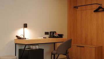 A compact room with a wooden desk, a chair, a small stool, a hanging coat rack, and a wardrobe.