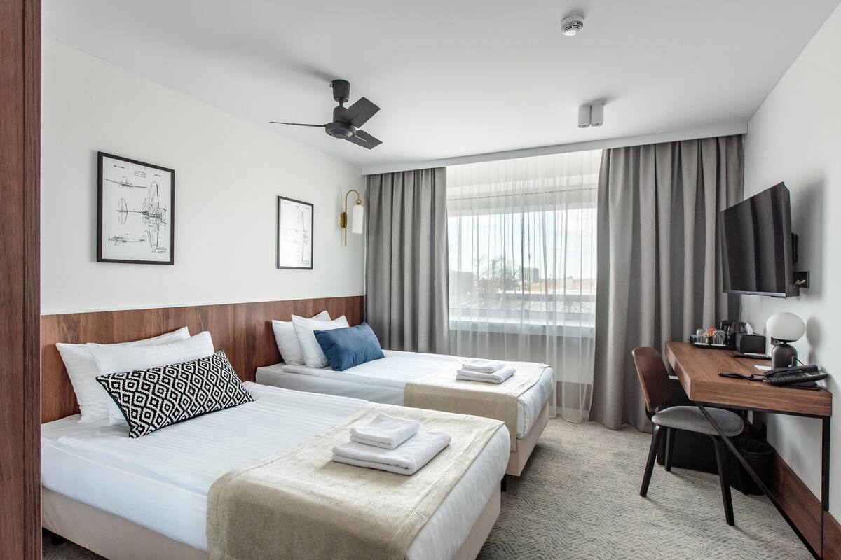 A hotel room with two beds, a desk, a chair, a television, and a window with curtains.