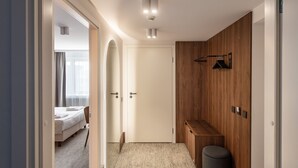 Una habitación de hotel moderna con una cama, un armario de madera, una pequeña zona de estar y una puerta que da a otra habitación.