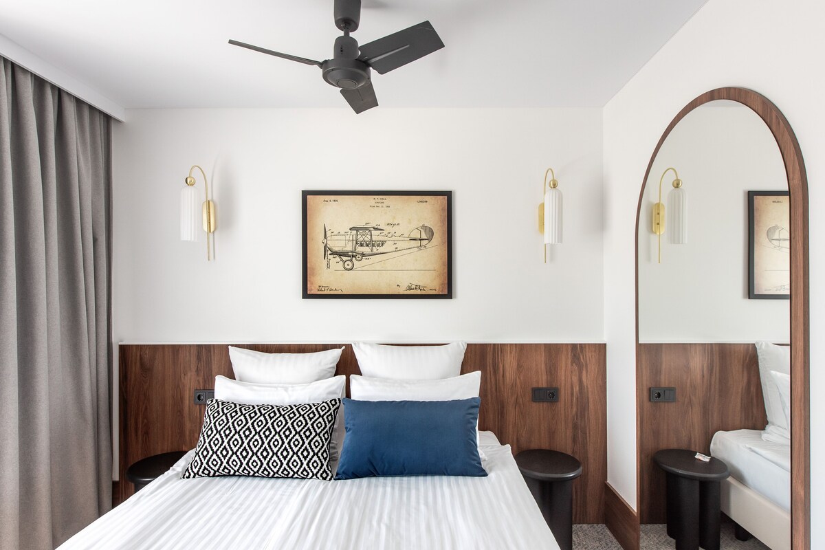 A hotel room with a bed, a ceiling fan, a framed blueprint on the wall, and two bedside tables.