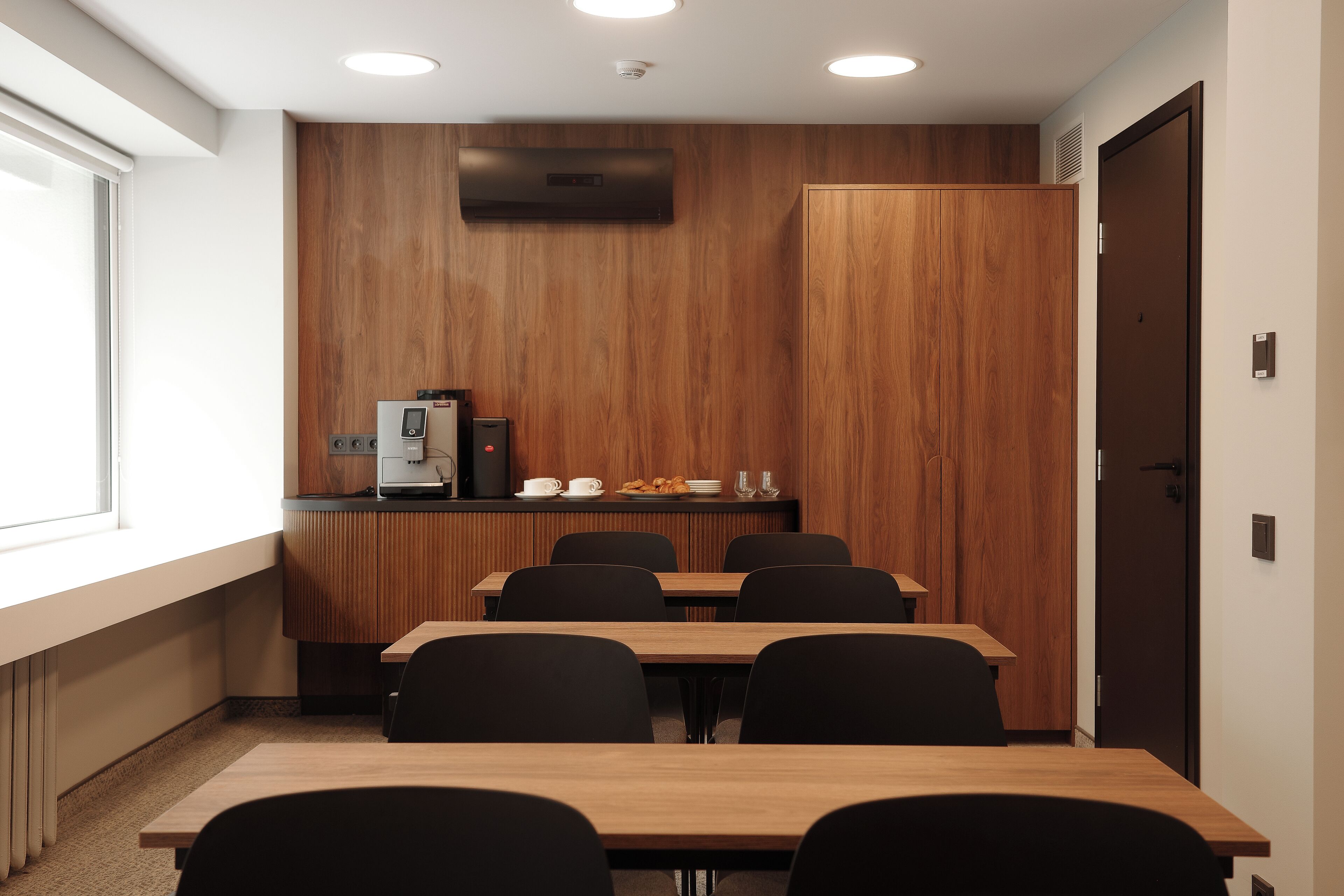 Ein Konferenzraum mit Holzwand, einer Kaffeestation und einer Tür.
