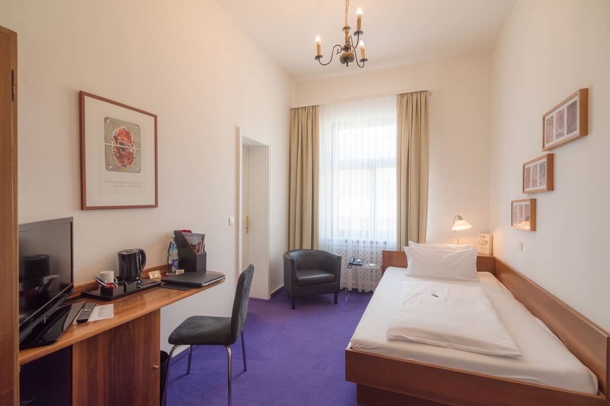 A hotel room with a bed, desk, chair, television, and a chandelier.