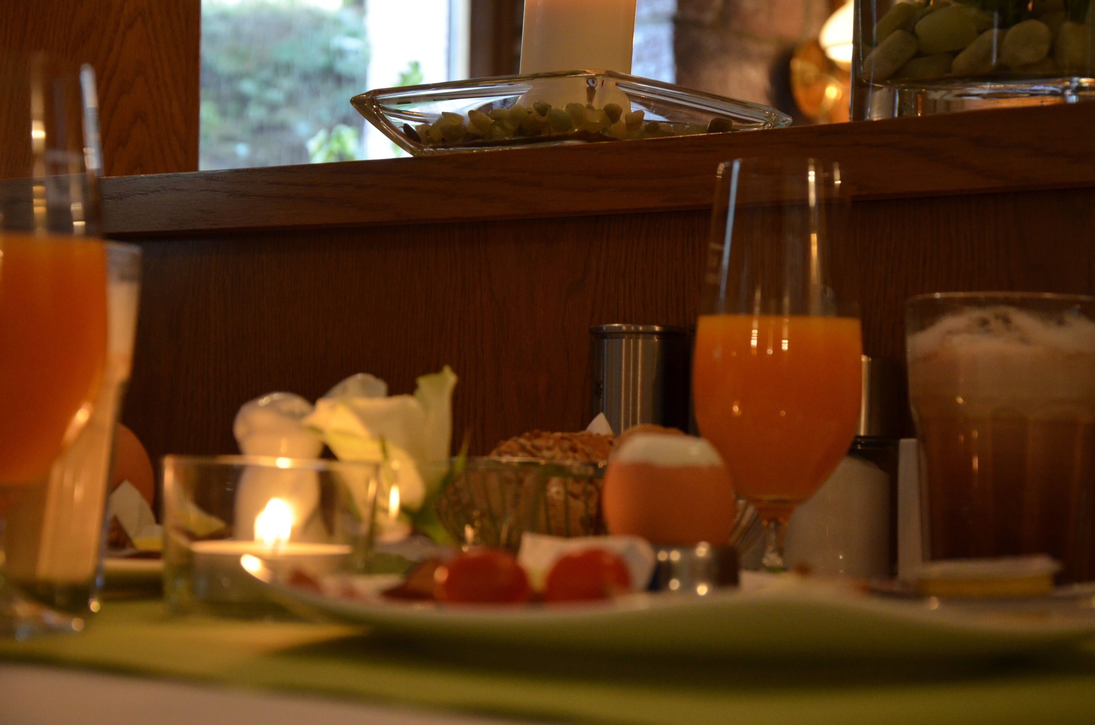 A breakfast table with various food items and drinks, including a glass of orange juice, a plate with strawberries, and a candle.