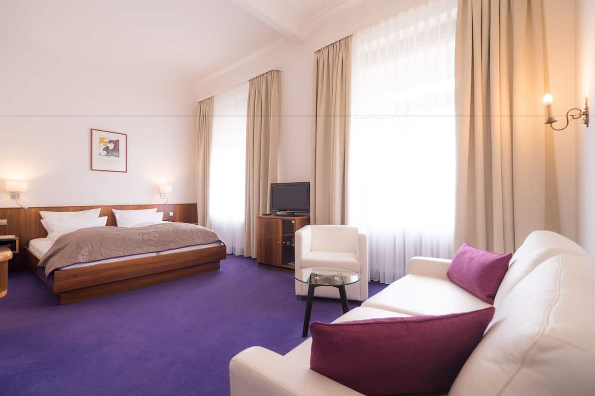 A hotel room with a bed, a sofa, a TV, and a small table.