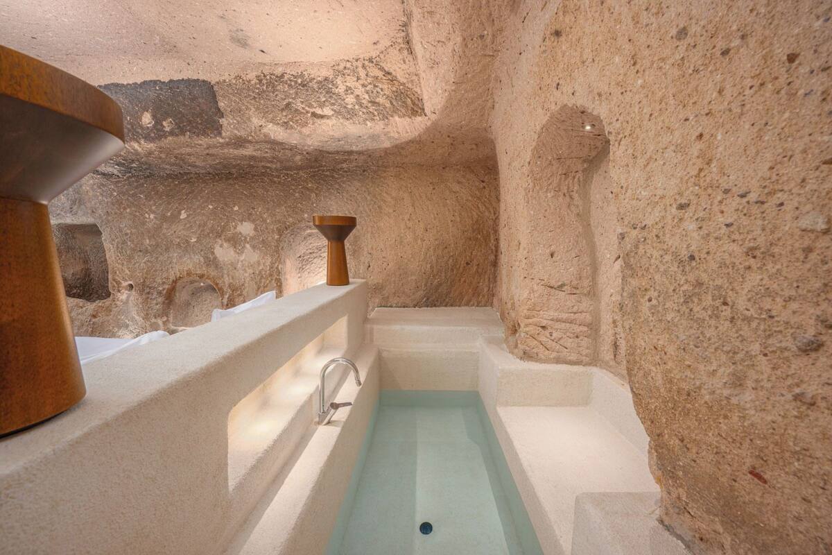 Una habitación de paredes de piedra con una bañera, un lavabo de madera y un lavamanos blanco.