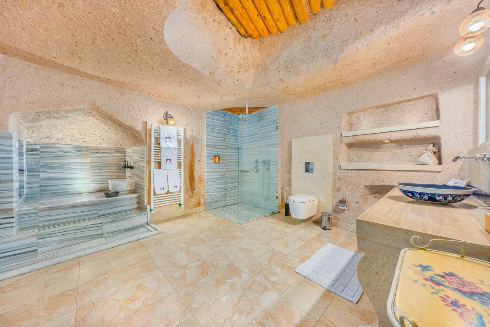 A bathroom with a stone wall, a glass shower enclosure, a white toilet, and a sink with a decorative bowl.