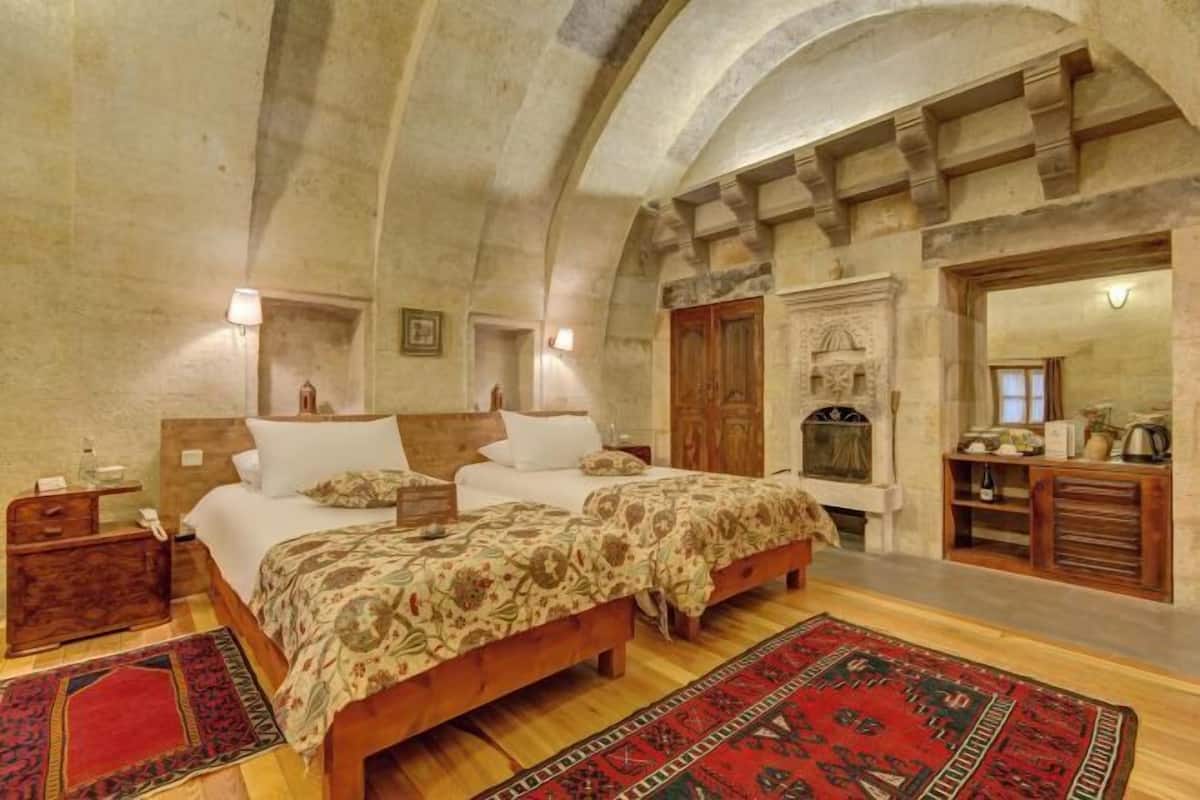 Un dormitorio con dos camas, cabeceros de madera, una chimenea y una pared de piedra.