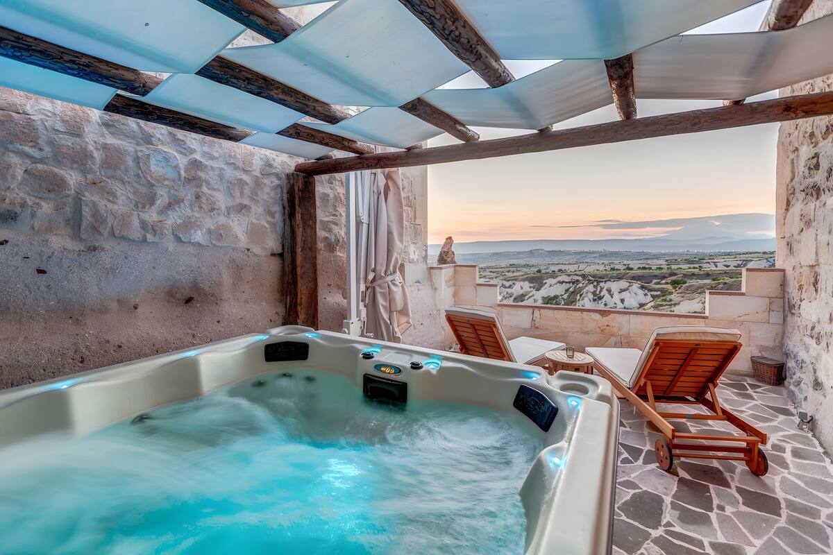 Habitación de paredes de piedra con jacuzzi, sillas de madera y vistas al paisaje.