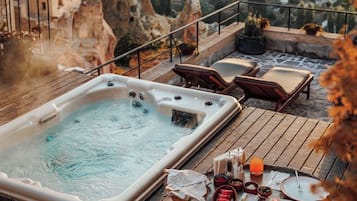A hot tub on a wooden deck with a table set for a meal, overlooking a landscape with rock formations and hot air balloons in the distance.