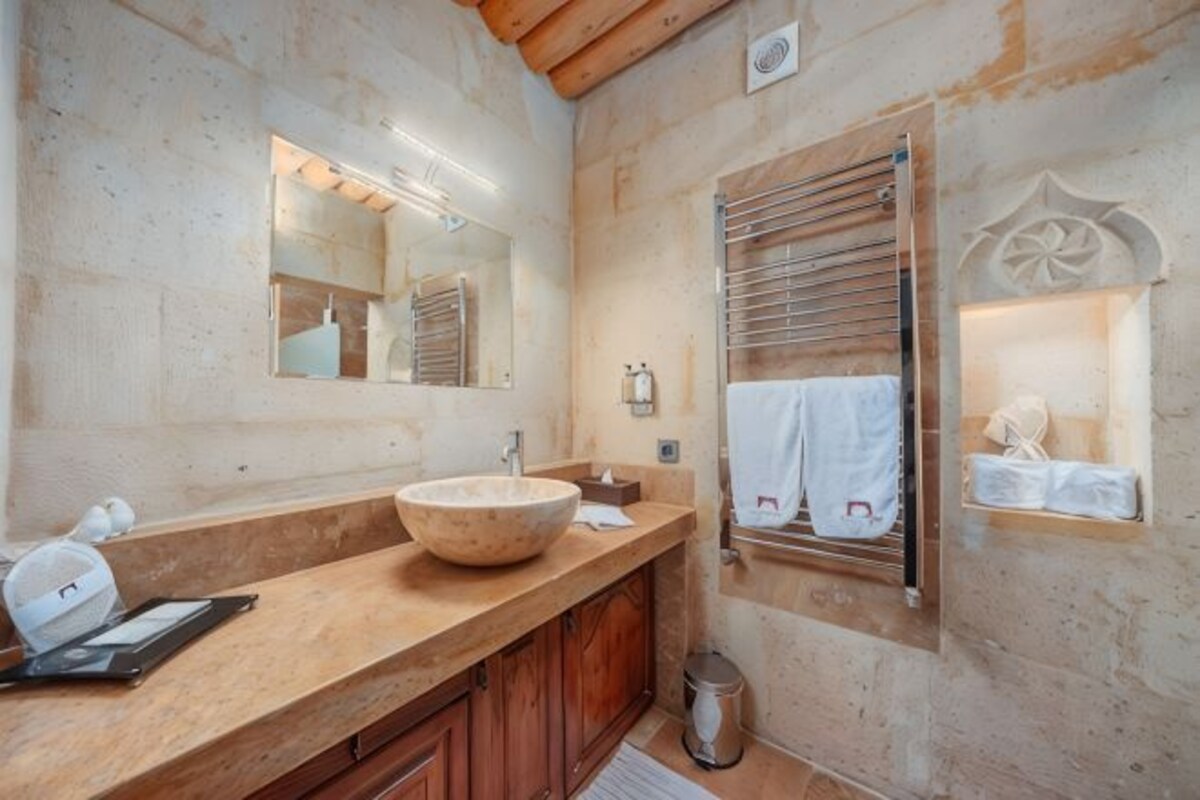 Un baño con tocador de madera, un espejo grande, toallero y una ventana pequeña con persianas.