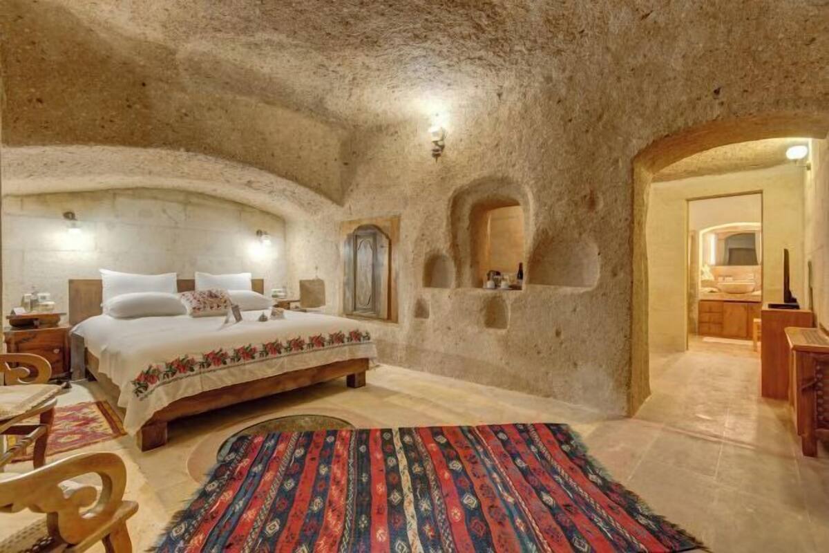 Un dormitorio con una cama grande, una silla de madera, una alfombra y una pared de piedra.