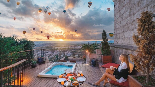 A rooftop terrace with a hot tub, dining table, and seating area overlooking a cityscape at sunset. - Hotel Taskonaklar Cappadocia - Special Class (Nevsehir)