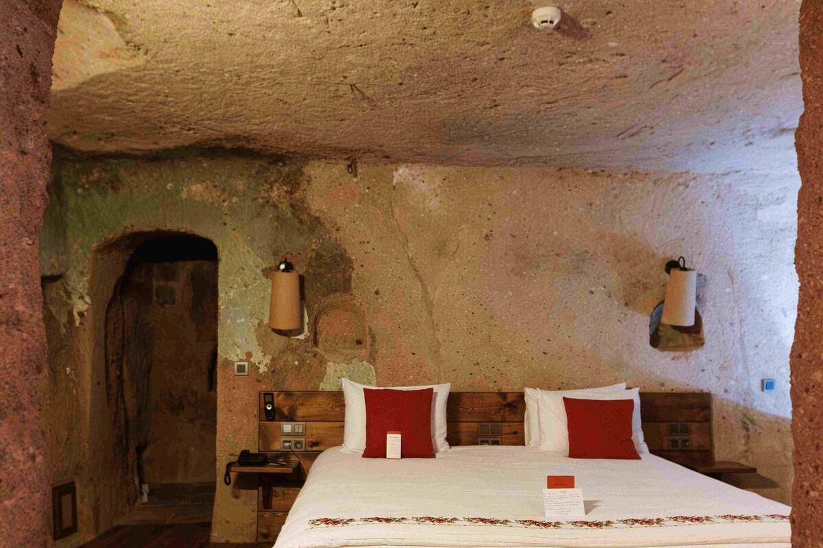 A rustic room with a bed, wooden floor, and a stone wall.