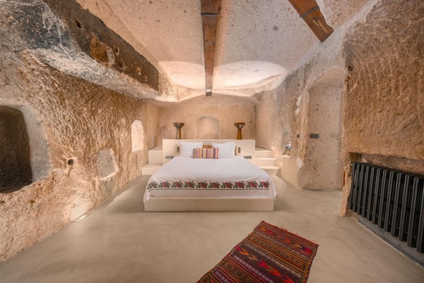 Une chambre avec un grand lit, une petite table et un radiateur. Les murs sont en pierre.