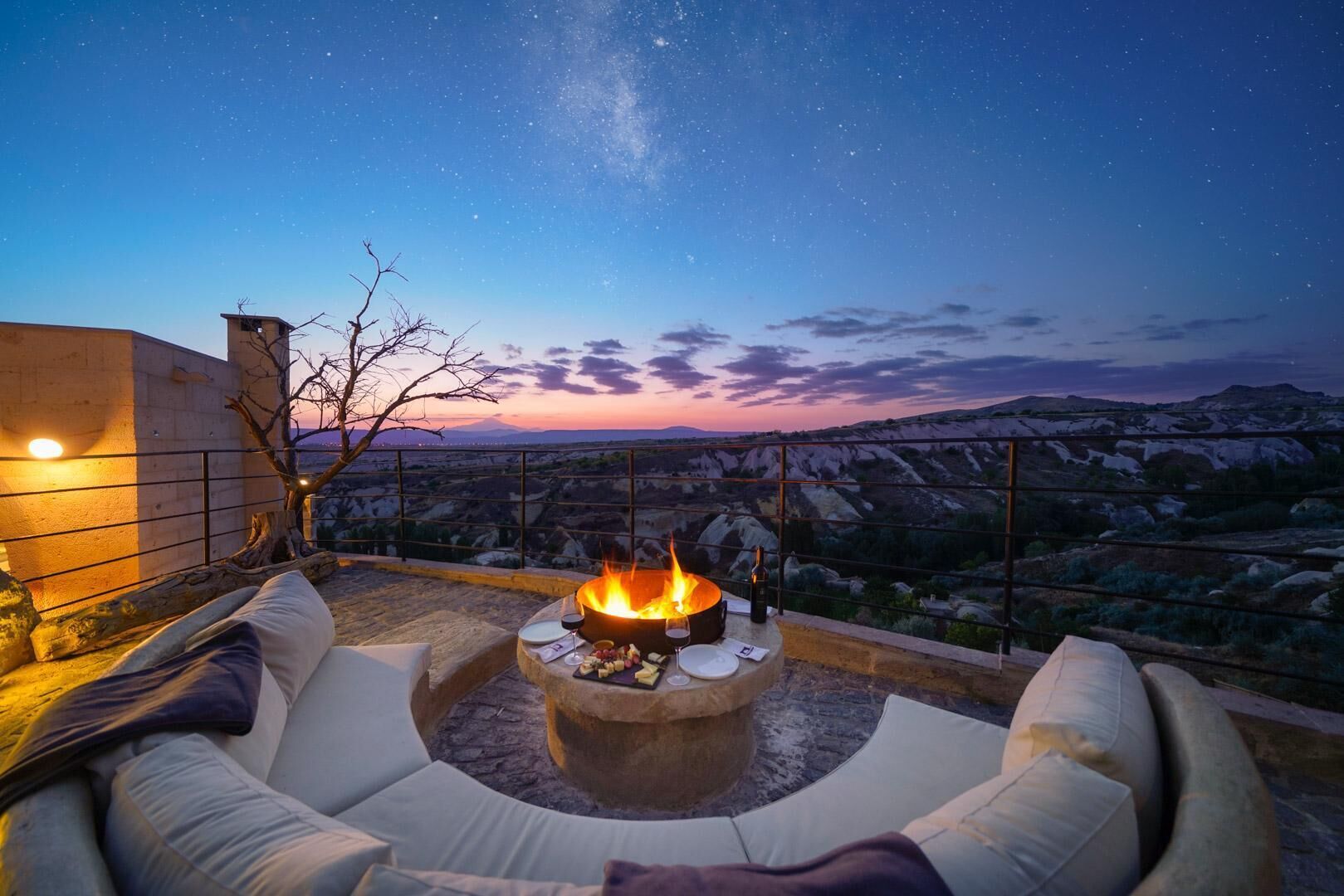 Un área de estar al aire libre con un brasero, cojines y vistas del paisaje.