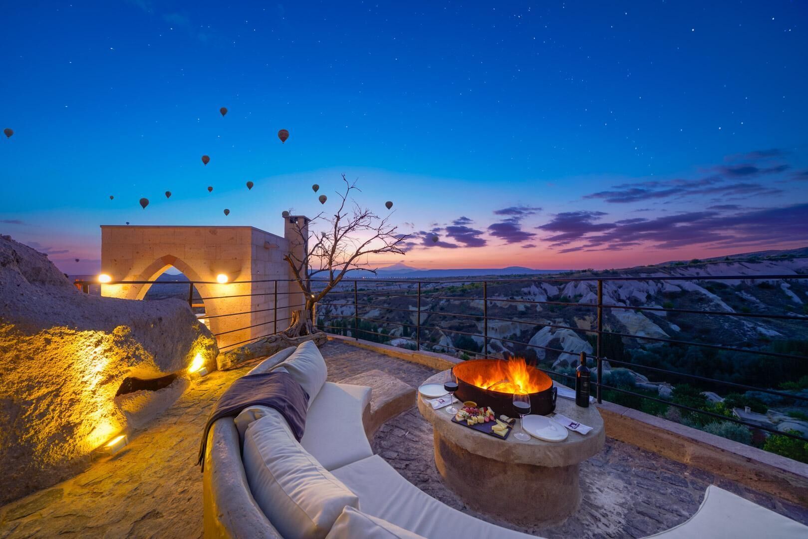 Una terraza en la azotea con chimenea de piedra, asientos acolchados blancos y vistas del paisaje.