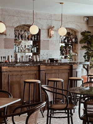 Un espace bar doté d’un comptoir en bois, de plusieurs tabourets et d’étagères remplies de bouteilles.