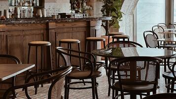 Zona de bar con taburetes de madera, mostrador con diferentes botellas y una planta grande en maceta.