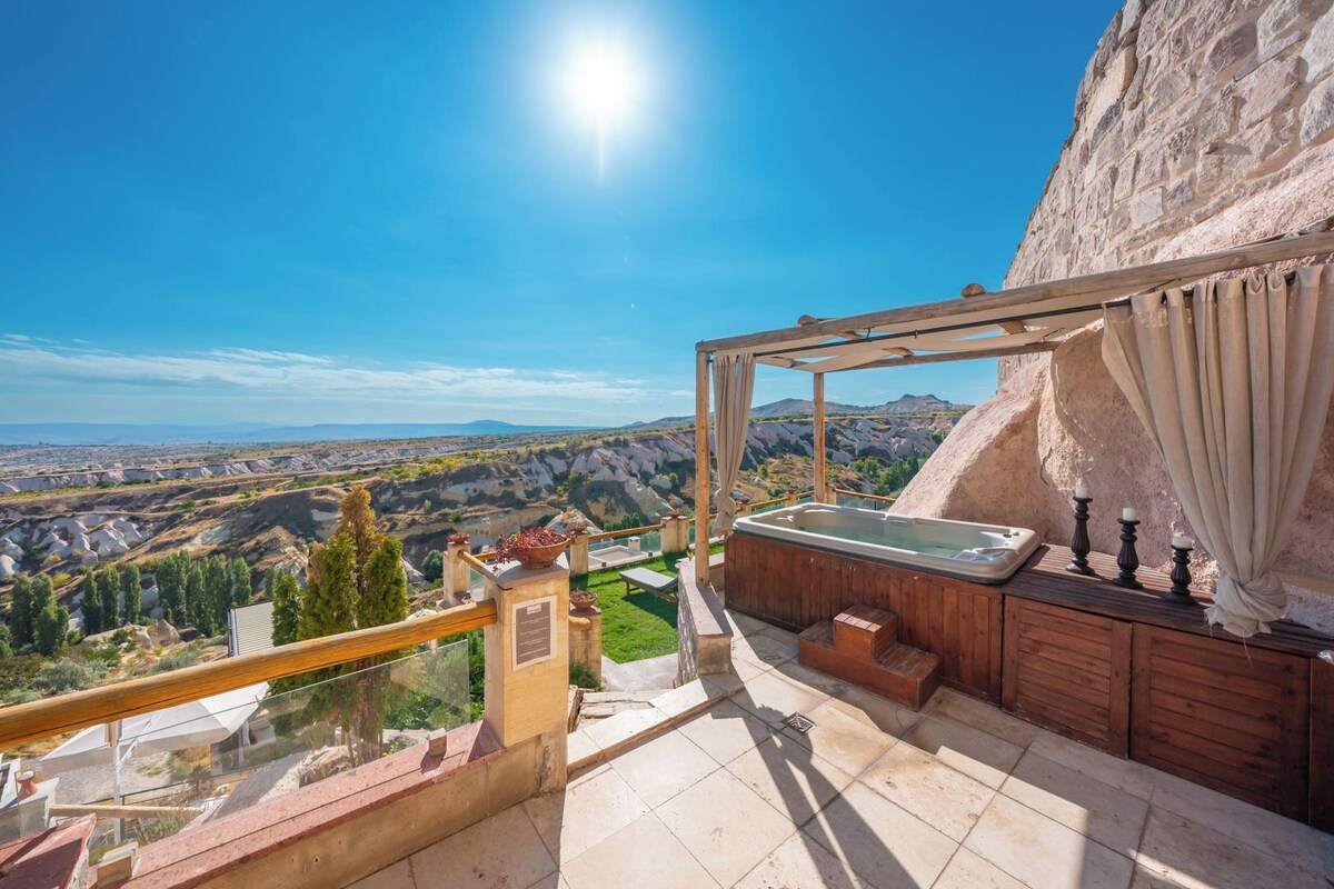 A balcony with a hot tub, wooden furniture, and a view of a mountainous landscape.