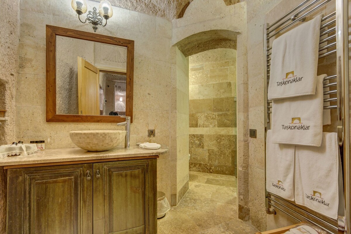 A bathroom with a wooden vanity, a large mirror, a stone shower, and multiple towels hanging on a rack.