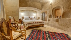 A bedroom with a rustic stone wall, a wooden bed, a chair, a table with a vase, and a rug. - Hotel Taskonaklar Cappadocia - Special Class (Nevsehir)