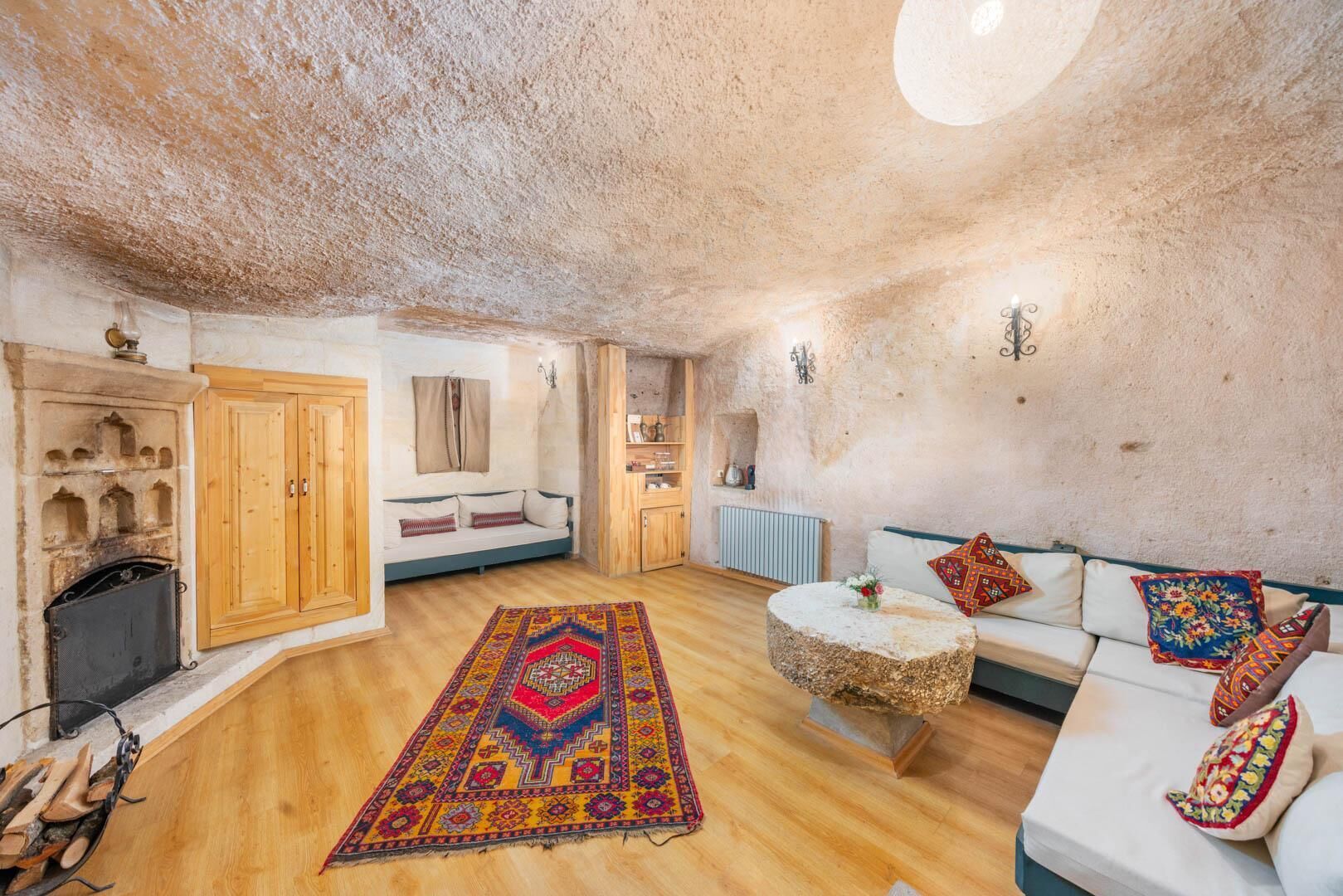 A cozy living room with a stone ceiling, wooden furniture, a patterned rug, and a fireplace.