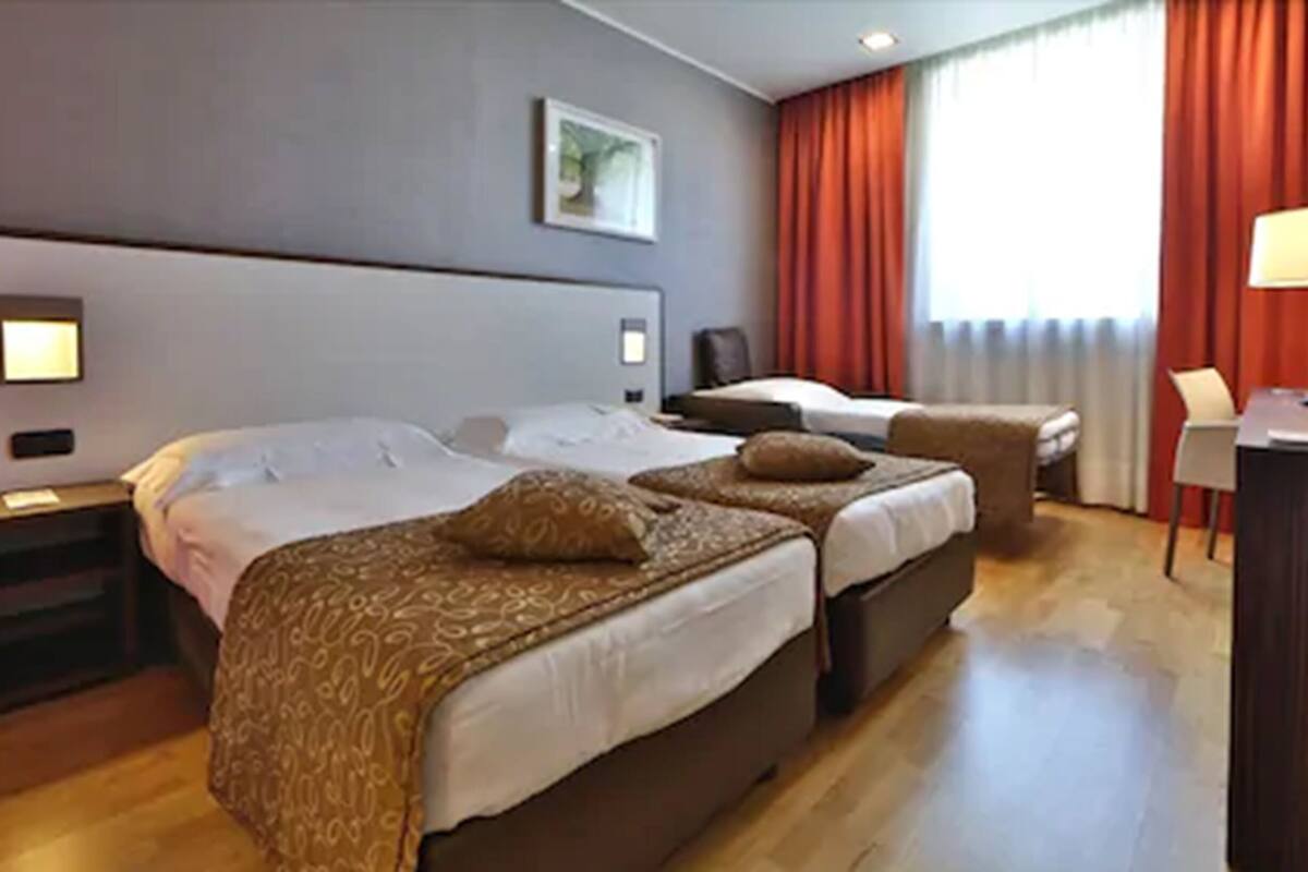 A hotel room with two beds, a desk, a chair, and a window with curtains.