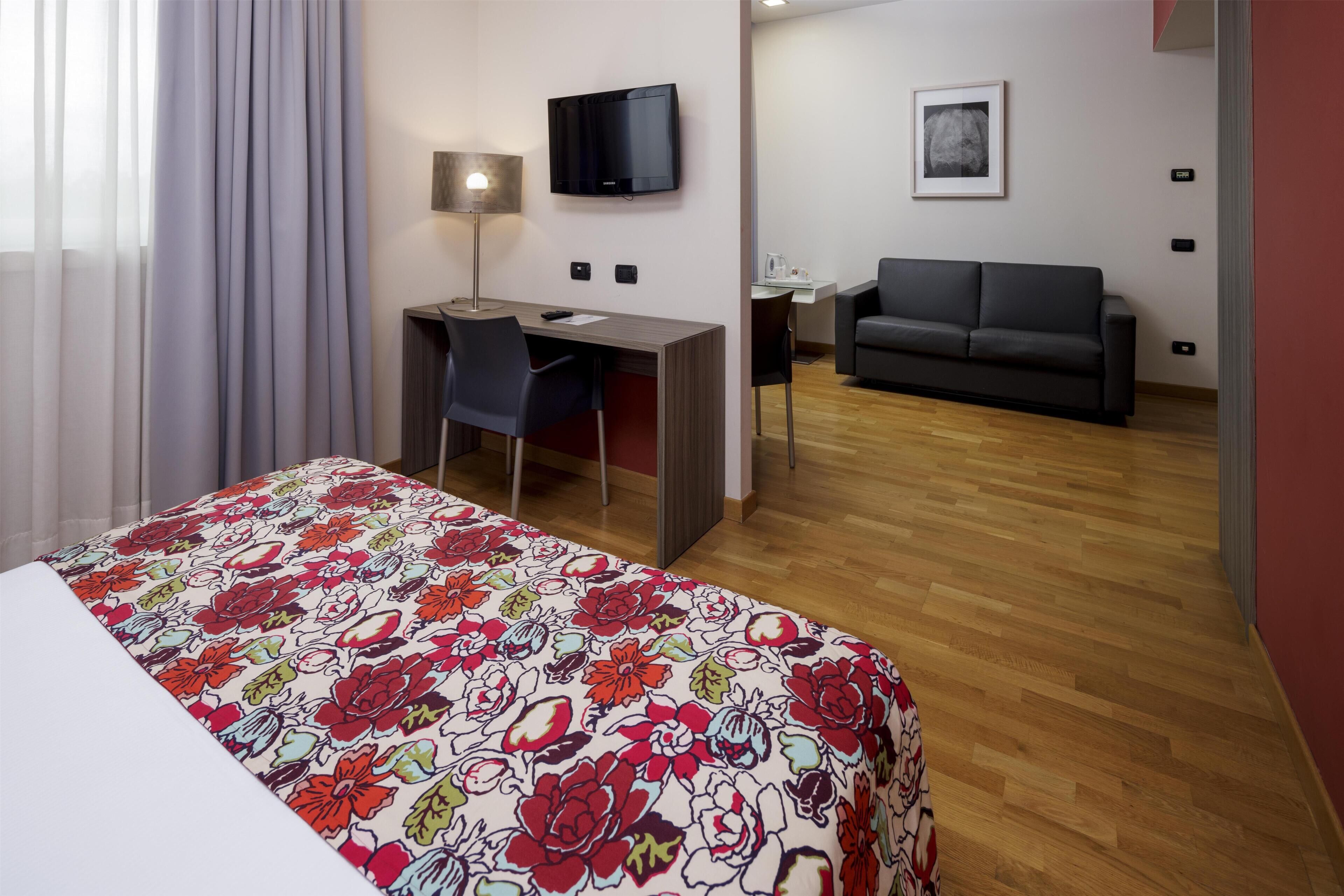 Ein Hotelzimmer mit Bett, Schreibtisch, Sessel, Fernseher, Sofa und einem kleinen Tisch.