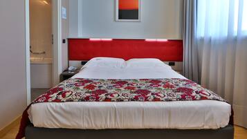A hotel room with a large bed, a red headboard, a nightstand, a telephone, and a painting on the wall.