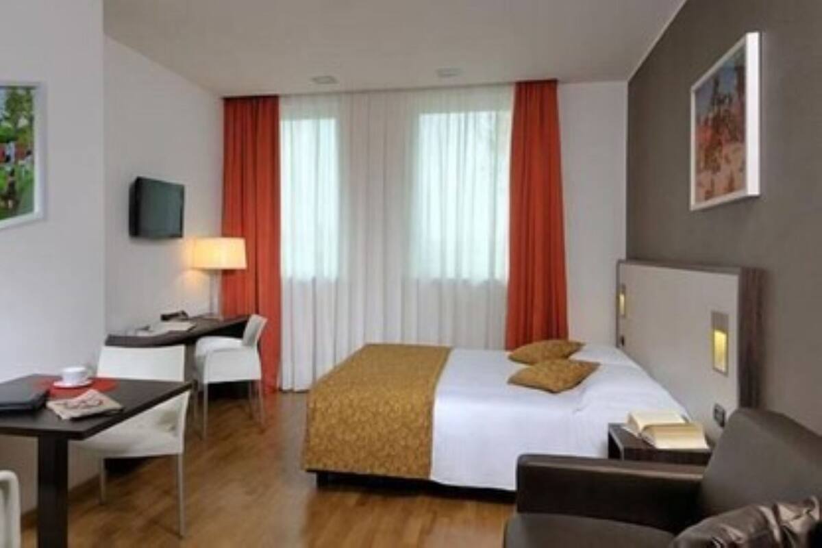 A hotel room with a bed, a desk, a chair, a TV, and a painting on the wall.