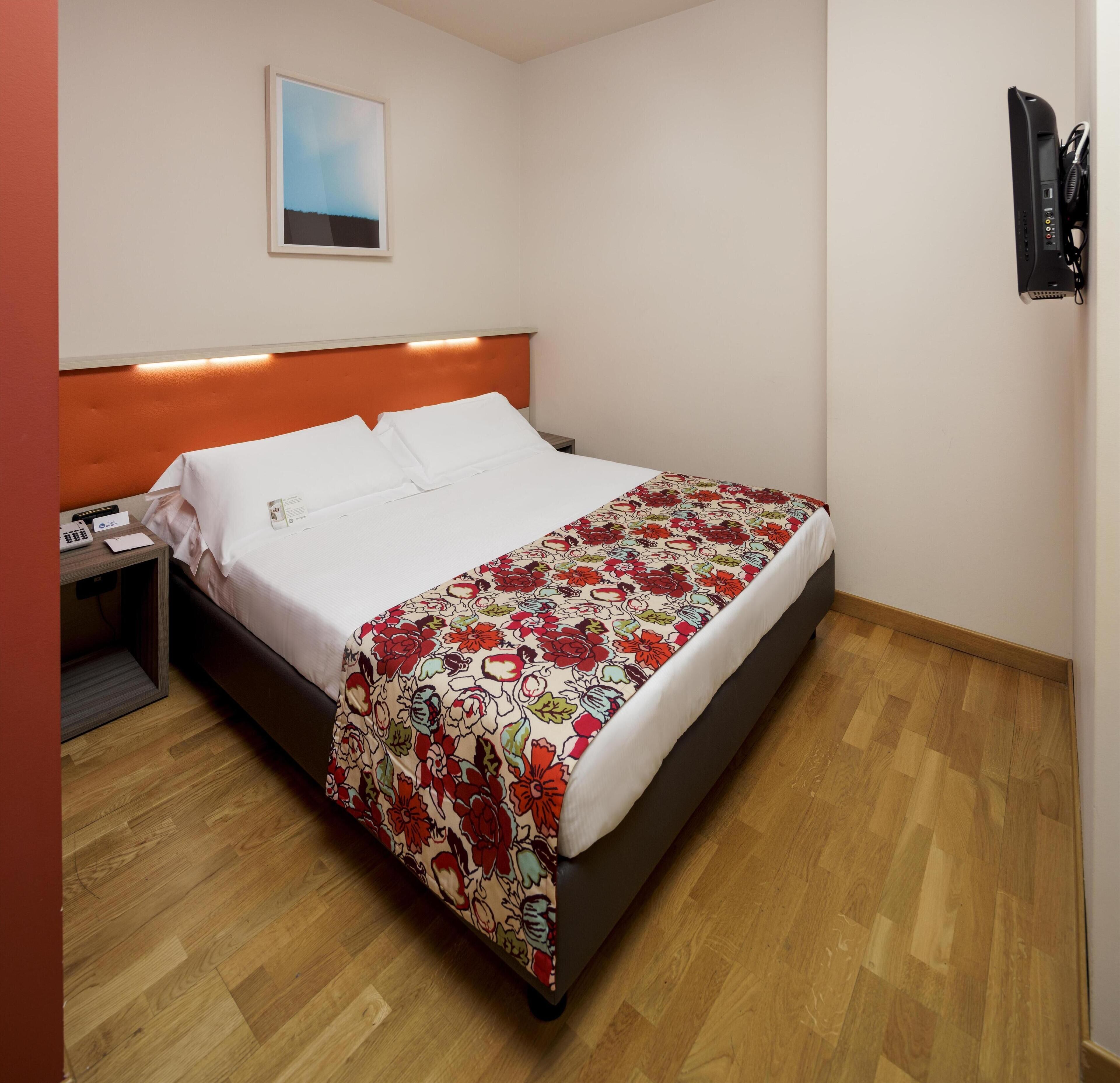 A hotel room with a bed, a nightstand, a telephone, and a wall-mounted TV.