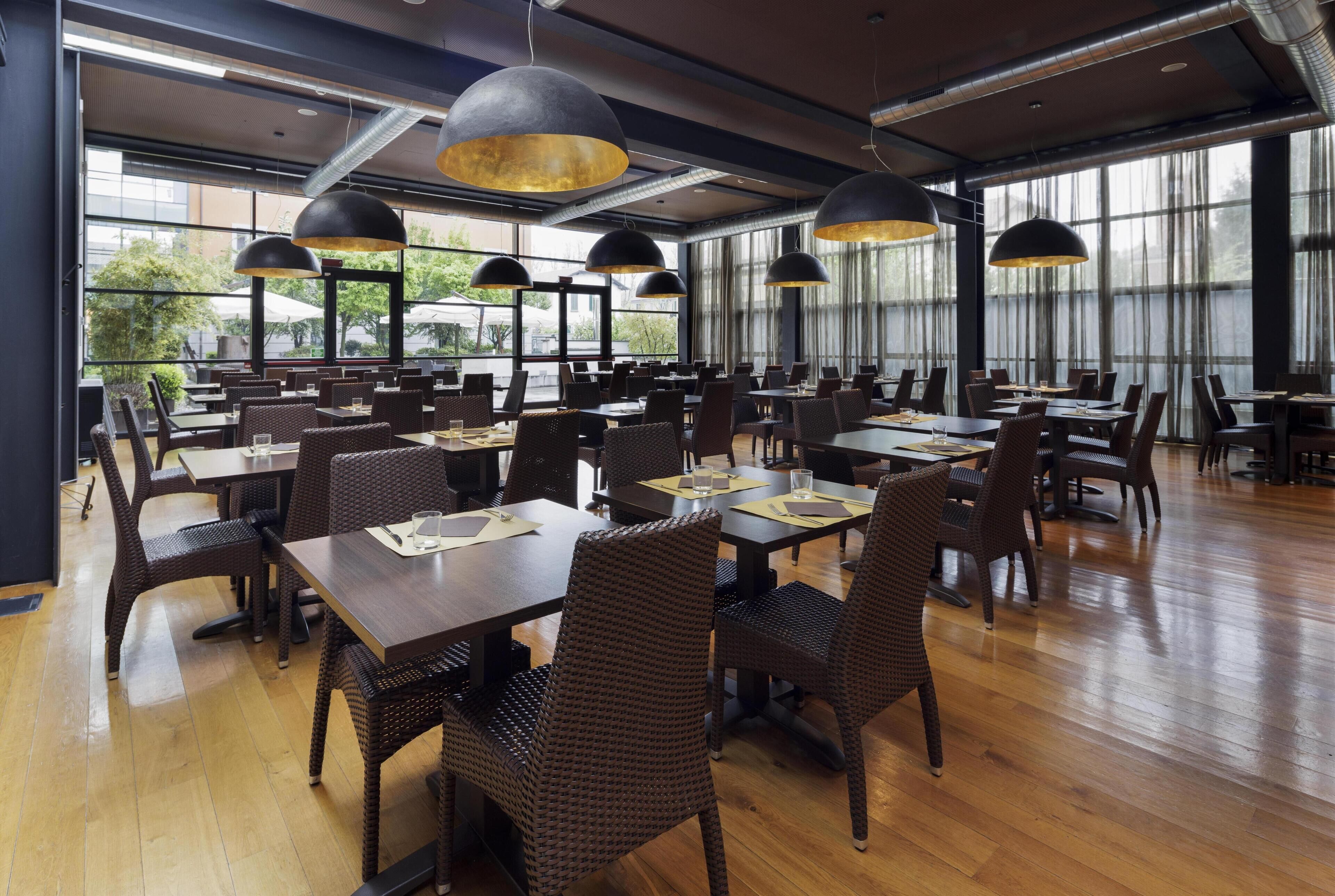 A spacious restaurant with high ceilings, large windows, and modern pendant lighting.